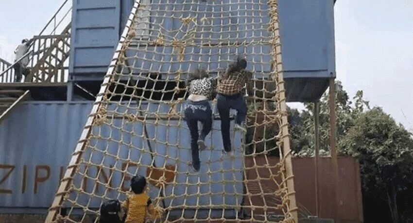 Visitors climbing a rope net course on shipping containers at the adventure zone of Madhavgarh Farms
