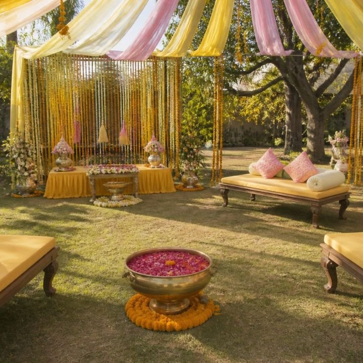 Mehndi and haldi ceremony setup with marigold strings and low seating on a farmhouse lawn
